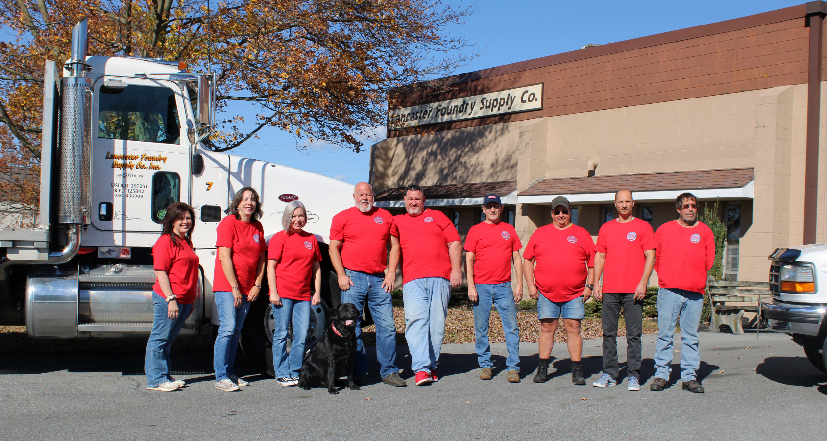 A group of Lancaster Foundry Supply Company employees wearing red shirts, standing next to company trucks outside of their work building