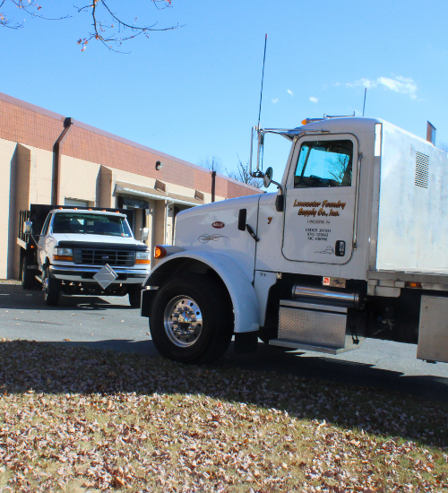 Two Lancaster Foundry Supply trucks parked outside building