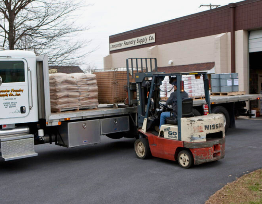 Employee driving skid loader, taking pallets off of a flatbed truck